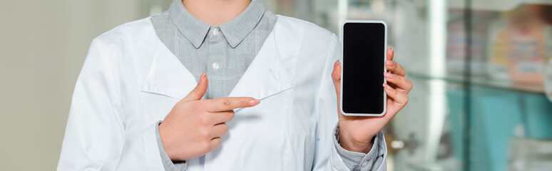 Cropped view of pharmacist pointing with finger at smartphone with blank screen, panoramic shot