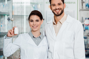 Fototapeta na wymiar Smiling pharmacists with pills looking at camera in drugstore