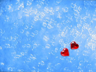 Two red hearts of lovers on a blue, blurred background with bokeh.