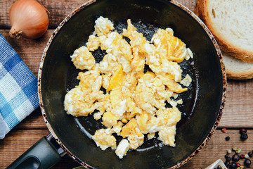 Top view on Scrambled eggs in a pan on a wooden countertop. The concept of preparing a meal of eggs, scrambled eggs.