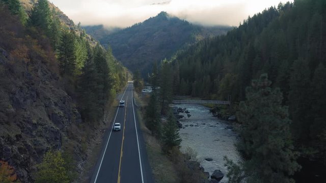 Aerial: Cars driving down a highway in a forest. Alongside it is a calm river. Nez Perce Clearwater National Forests, Idaho, USA