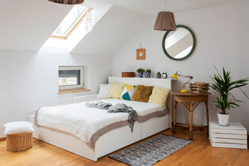Modern interior of bedroom in white color with double bed and yellow pillows in the attic. Mirror...