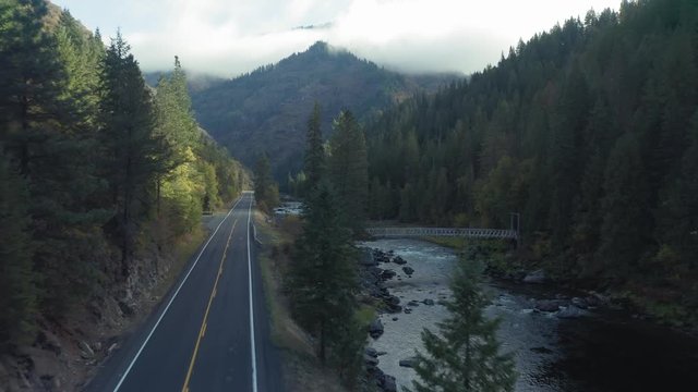 Aerial: Flying down highway in a forest. Alongside it is a calm river and bridge. Nez Perce Clearwater National Forests, Idaho, USA