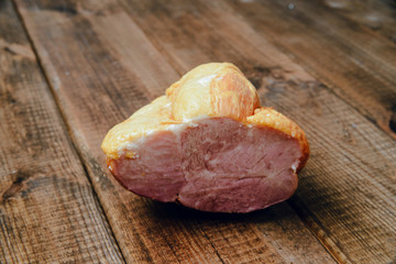 A piece of smoked ham on a wooden background. The concept of consuming cold meats with a meal.