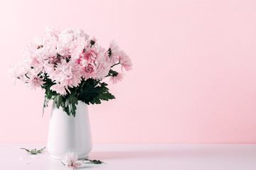 Fresh bouquet of pink flowers in vase on white shelf on pink wall background. Floral home decor.
