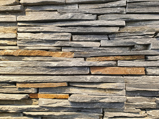Close-up view of an artificial wall made of stone slabs with natural multiple colors stacked on top of each other that looks similar to a real natural stone.