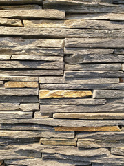 Close-up view of an artificial wall made of stone slabs with natural multiple colors stacked on top of each other that looks similar to a real natural stone.