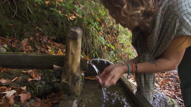 girl drinking a water from the forest wooden water trough at the autumn mountains forest