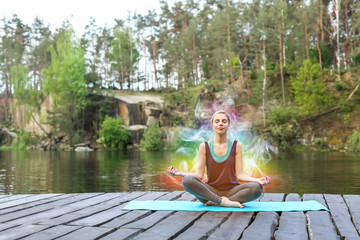 Beautiful young woman practicing yoga outdoors near river