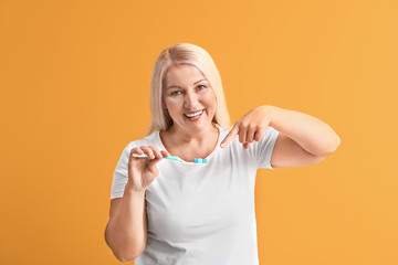 Mature woman with toothbrush on color background