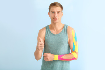 Sporty man with physio tape applied on arm showing thumb-up gesture against light background