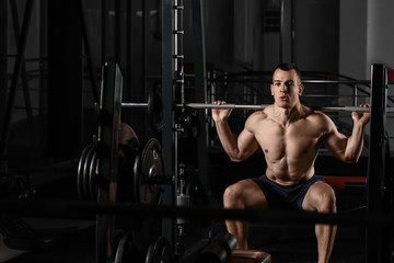 Fototapeta na wymiar Sporty muscular man training with barbell in gym