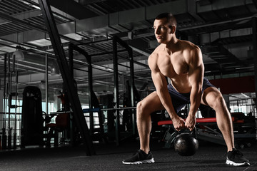 Fototapeta na wymiar Sporty muscular man training with kettlebell in gym