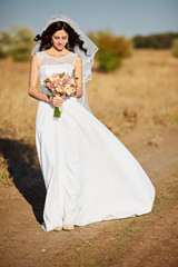 Fototapeta na wymiar Beautiful smiling bride wearing a natural flower wreath and standing in the golden summer fields