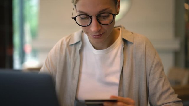 Zoom in to female in eyewear doing online transfer with debit card searching good offer purchases in web store connecting to home internet on laptop, concept of verification cvv operation