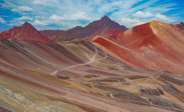 Landscape of hiking scene at Rainbow Mountain at  Vinicunca Valley. Apu Ausangate is behind. All rocks, mountains and sand is invaded by red colors. Cusco Region, Peru