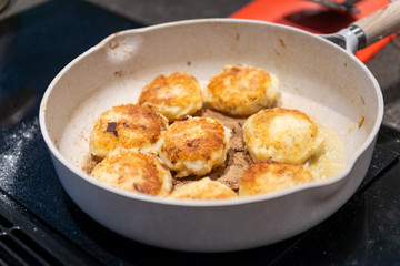 Round patty style fishcakes frying in butter on a white skillet. The fish cakes are round and golden brown they contain codfish, salt cod, savory, butter and potatoes and are golden brown. 