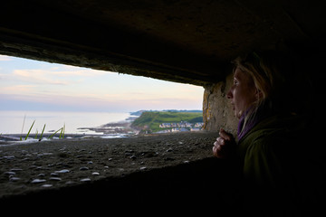Young Woman looking out of a bomb shelter in the Normandy in France over the ocean and coast