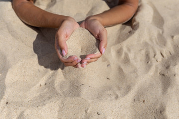 Close-up of female hand releasing dropping sand. Sand flowing through the hands. Summer beach holiday vacation concept