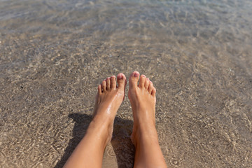 Tanned legs of a girl against the sea on the sand. Concept of rest on the sea. Female feet on white sandy beach
