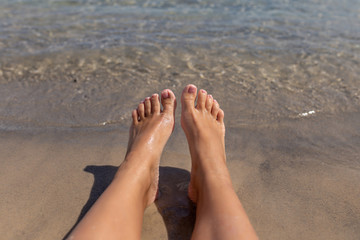 Tanned legs of a girl against the sea on the sand. Concept of rest on the sea. Female feet on white sandy beach