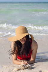 Young woman smiling lie down on the beach face down and wearing a hat