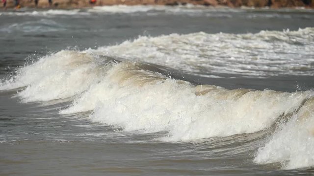 Close up of wave on muddy beach with blur tourists background, high speed camera, super slow motion, 180 FPS.