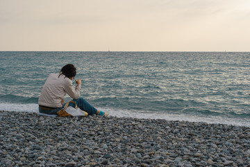 a woman sits on a shingle by the sea and looks into the distance. focus on the woman