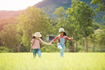 Two little girl carrying a backpack and wearing a hat. Running around in the grassland Children walk and enjoy the surrounding nature. She enjoys traveling in the summer.