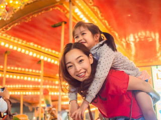 Fototapeta na wymiar happy asia mother and daughter have fun in amusement carnival park with farris wheel and carousel background