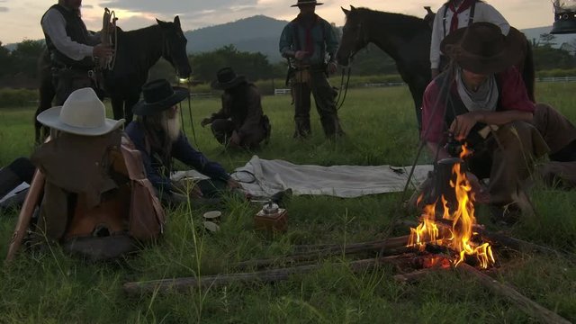 Cowboy groups stopped camping and rested and brewed coffee. Some people are use knives to burn fire. Some people are rested at the horse saddles.