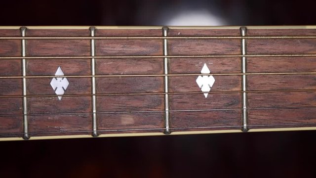 Pan along neck of used steel-stringed acoustic guitar, close-up