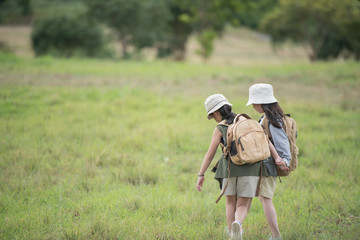 Two little girl carrying a backpack and wearing a hat. Running around in the grassland Children walk and enjoy the surrounding nature. She enjoys traveling in the summer. travel and adventure concept.