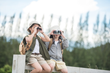 Two asia little girl carrying a backpack and wearing a hat. Use binoculars and take pictures Children enjoy the surrounding nature. She enjoys traveling in the summer. travel and adventure concept.