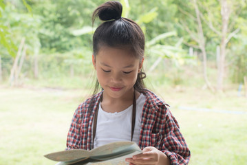 Happy asian kid girls to summer travel trip with green background. She traveled alone with checks map to find directions. Travel and adventure concept.
