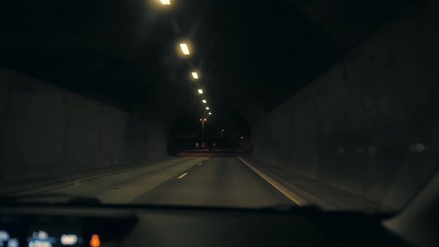 Cinematic footage of inside a car that is driving out of a tunnel on the highway in the middle of the night, lights lighting up the darkness, dashboard barely visible, natural camera movement