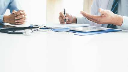 Patient listening intently to a male doctor explaining patient symptoms or asking a question as they discuss paperwork together in a consultation