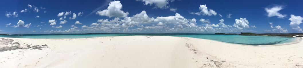 Fototapeta na wymiar Panoramic image of white sand and turquoise waters underneath a bright blue sky with white puffy clouds in the Sea of Abaco in the Bahamas