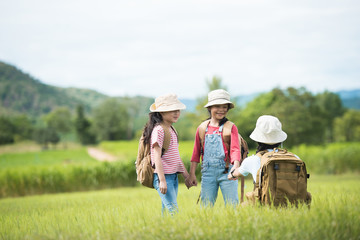 The three girls are in the meadow. Children have a backpack and a hat. In the countryside, children enjoy traveling in the summer. Travel and adventure concepts