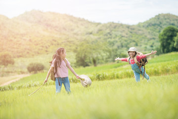 Two children carrying a backpack in their backs and wearing a hat, standing under a tree in the countryside. She walked and enjoyed the surrounding nature. She enjoys traveling during the summer.