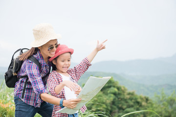 Fototapeta premium Mother and daughter stand on the mountain, pointing their hands forward. With a backpack and wearing a hat, standing, checking the map, with mountains in the background. Travel and adventure concepts