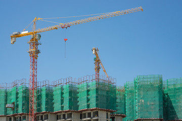 Upward view of precast building cover by green net, large tall Tower Crane moving machine in...