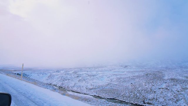 Side view, driving trough snowy, icy landscape road in winter. Mountain road in Iceland with cloudy sky. View from inside car, Westfjord, Iceland