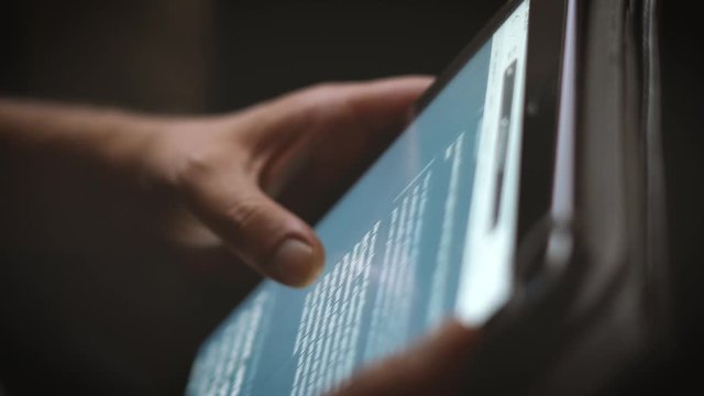 Shooted in slow motion showing man's hands browsing social media or playing with a mobile tablet at evening (dark space)