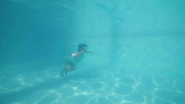 Active brave little girl swimming underwater in pool.