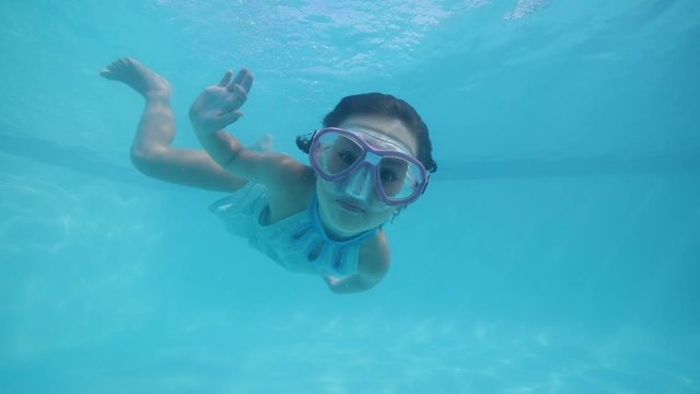 Child girl in swimming mask diving underwater in pool and looking at camera.