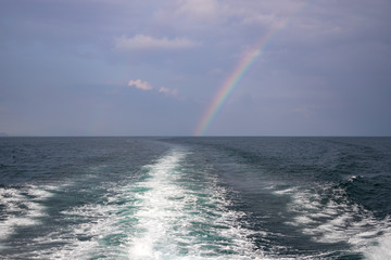 Waves from a boat sailing with rainbow in the backdrop in andaman sea off the coast of Thailand in Krabi Town