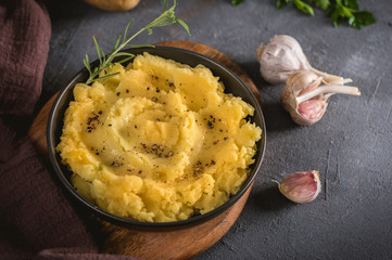 Mashed potatoes in bowl on wooden table with herbs and spices