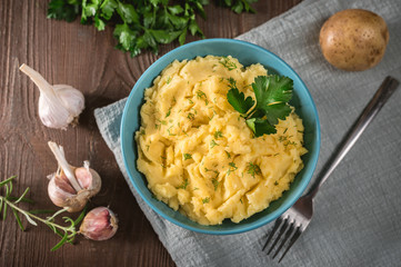 Mashed potatoes in bowl on wooden table with herbs and spices