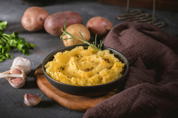 Mashed potatoes in bowl on wooden table with herbs and spices